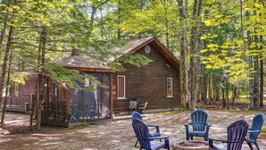 A rustic cabin with a porch, surrounded by trees and a fire pit with chairs. - Near Beach & Trails! Lake Winnipesaukee Cabin (Moultonborough)
