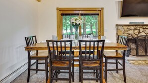 A dining area with a wooden table and chairs, a vase of flowers, and a stone fireplace. - Near Beach & Trails! Lake Winnipesaukee Cabin (Moultonborough)