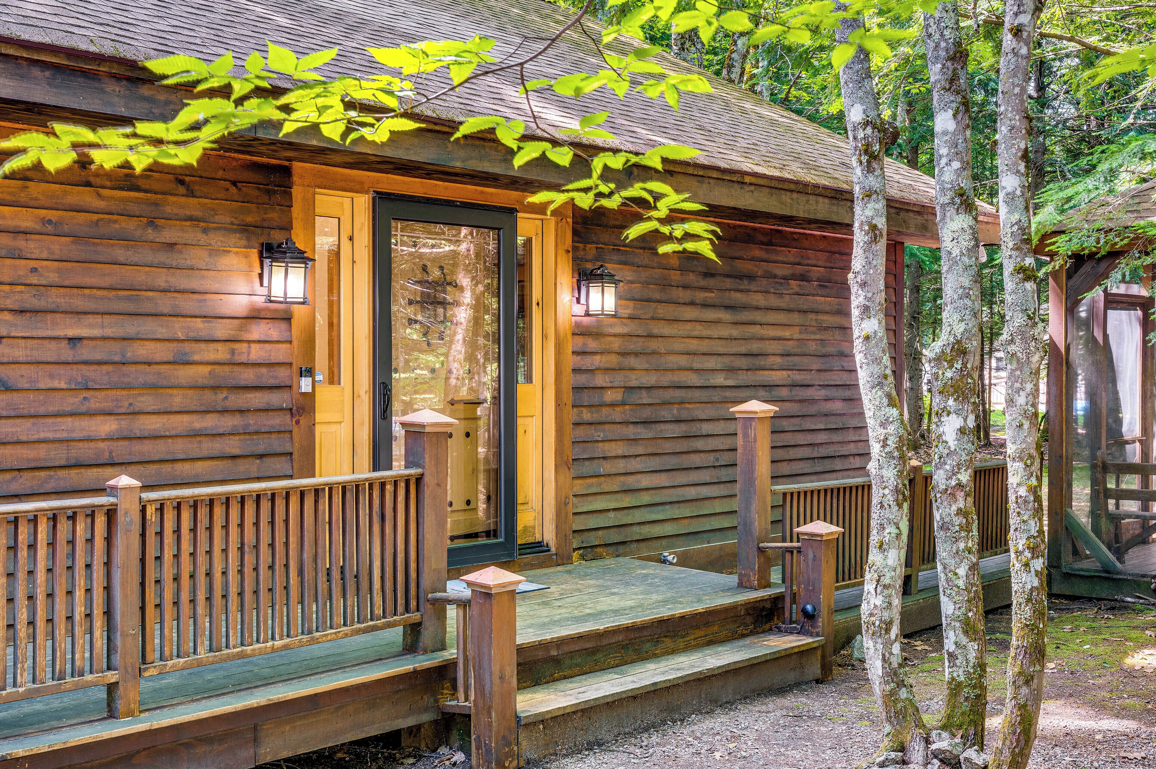 A wooden cabin with a porch, a door, and two lantern-style lights.