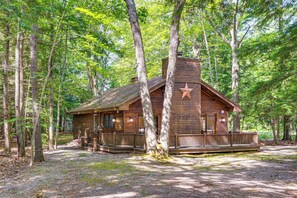 Eine rustikale Holzhütte mit Veranda, umgeben von hohen Bäumen.