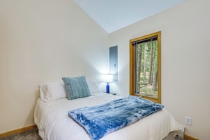 A bedroom with a bed, a window with a view of trees, a bedside lamp, and a wall-mounted light. - Near Beach & Trails! Lake Winnipesaukee Cabin (Moultonborough)