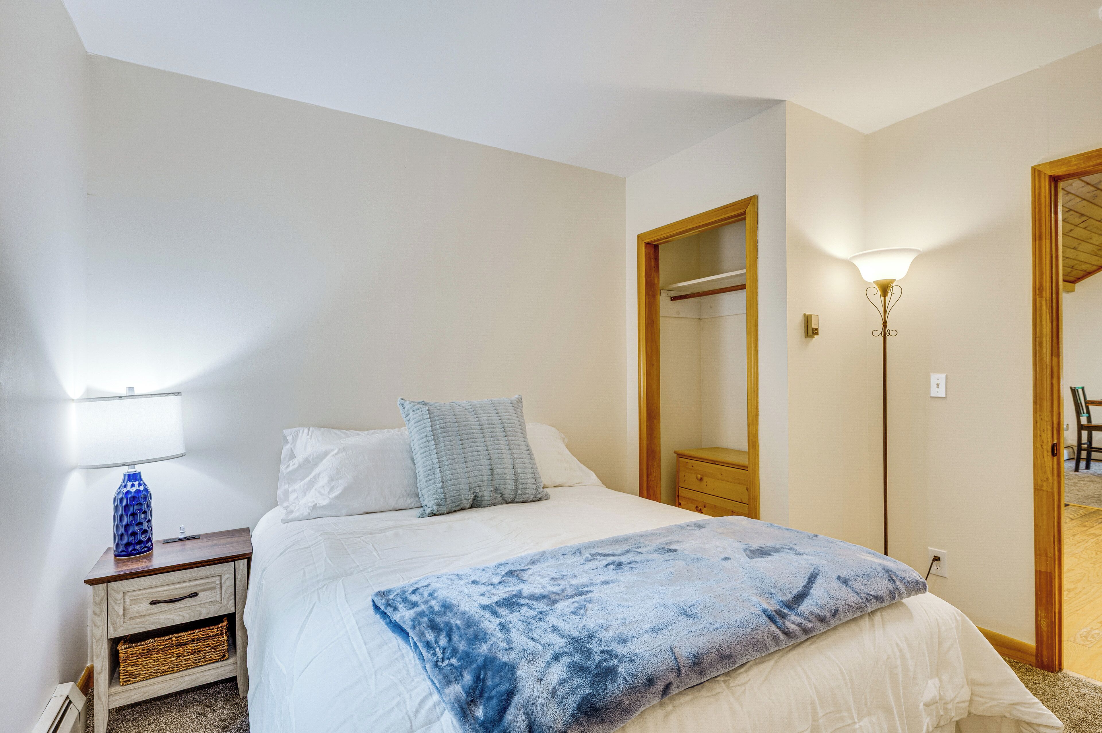 Un dormitorio con cama, mesita de noche, lámpara y espejo.