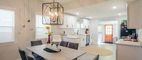 A modern kitchen with white cabinetry, a central island, and a dining area with a table and chairs.