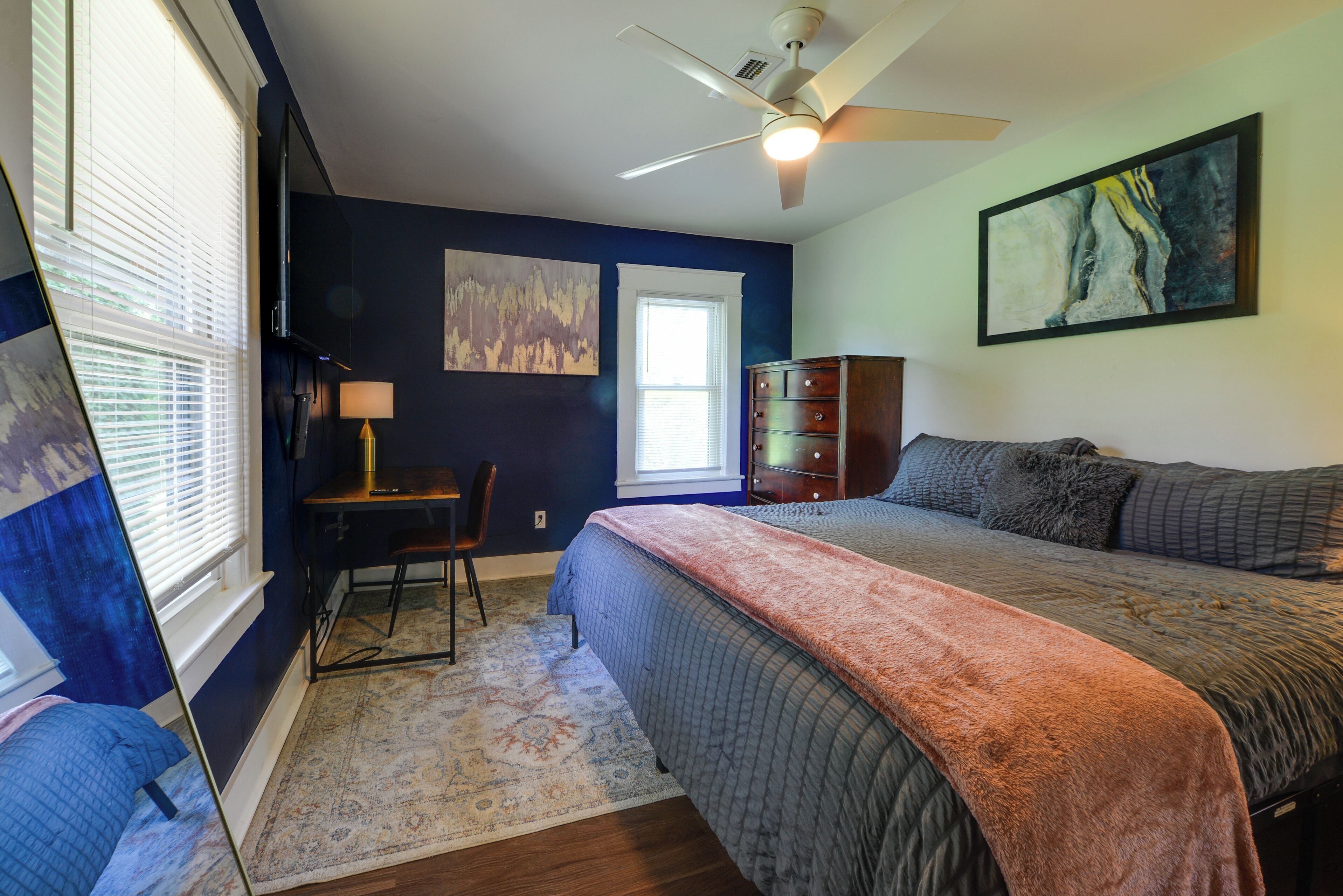 A bedroom with a bed, a desk, a chair, a dresser, and a ceiling fan.