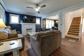 A living room with a fireplace, a ceiling fan, and a staircase leading to another level. - 1 Mi to Uncg & Dtwn! Group Retreat w/ Private Yard (Greensboro)