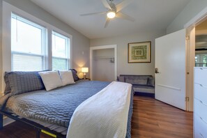 A bedroom with a bed, a ceiling fan, a bedside table with a lamp, a gray sofa, and a door. - 1 Mi to Uncg & Dtwn! Group Retreat w/ Private Yard (Greensboro)