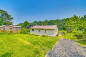 A single-story house with a front yard, a gravel driveway, and a backdrop of trees and hills. - Waterfront Getaway: Sunroom, 2 Decks, Golf Course (Wolcott)