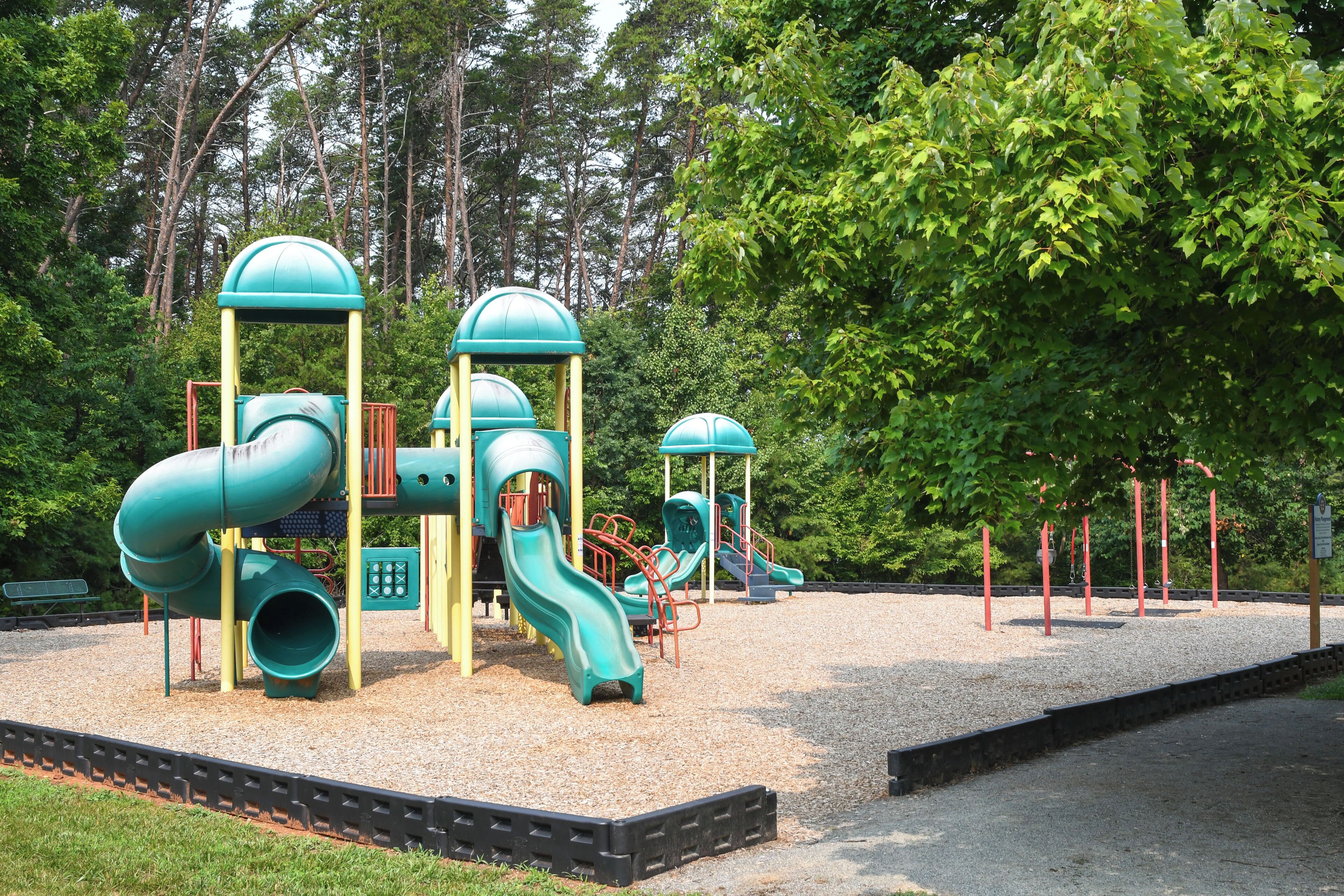 A playground with multiple slides and climbing structures surrounded by trees.