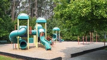 A playground with multiple slides and climbing structures surrounded by trees.