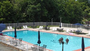 Una piscina rettangolare con recinzione bianca, circondata da sdraio e ombrelloni.