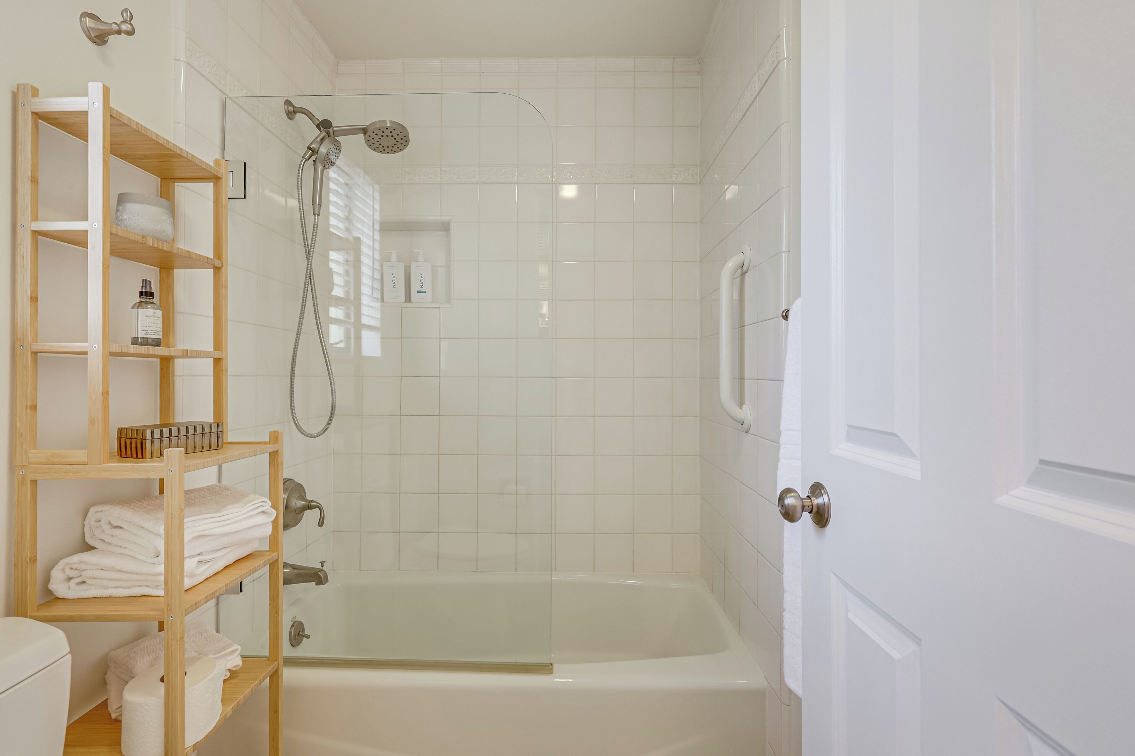 A bathroom with a bathtub, a shower, and a toilet. There are shelves with towels and toiletries.