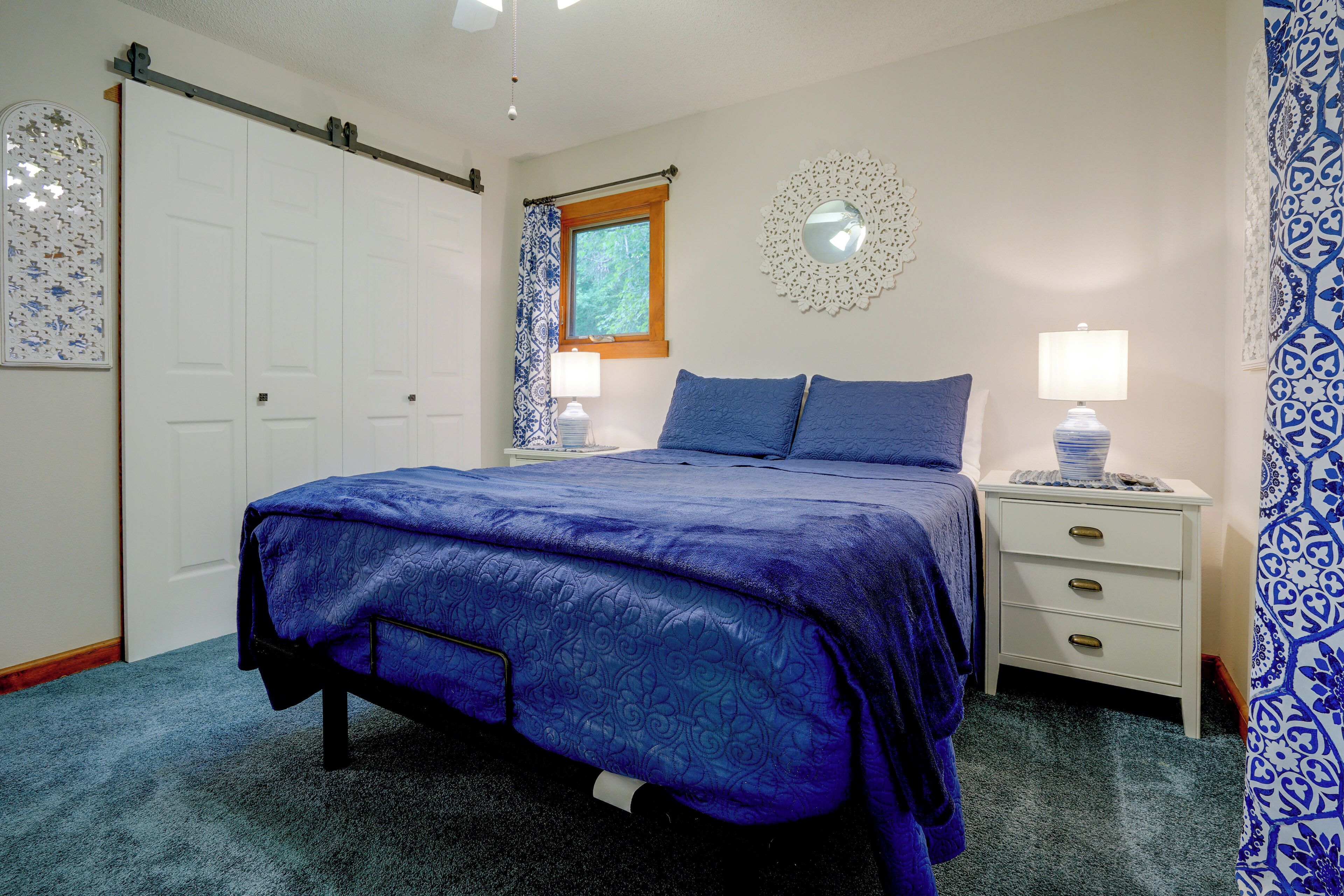 A bedroom with a bed, a nightstand, a dresser, a window with curtains, and a door.