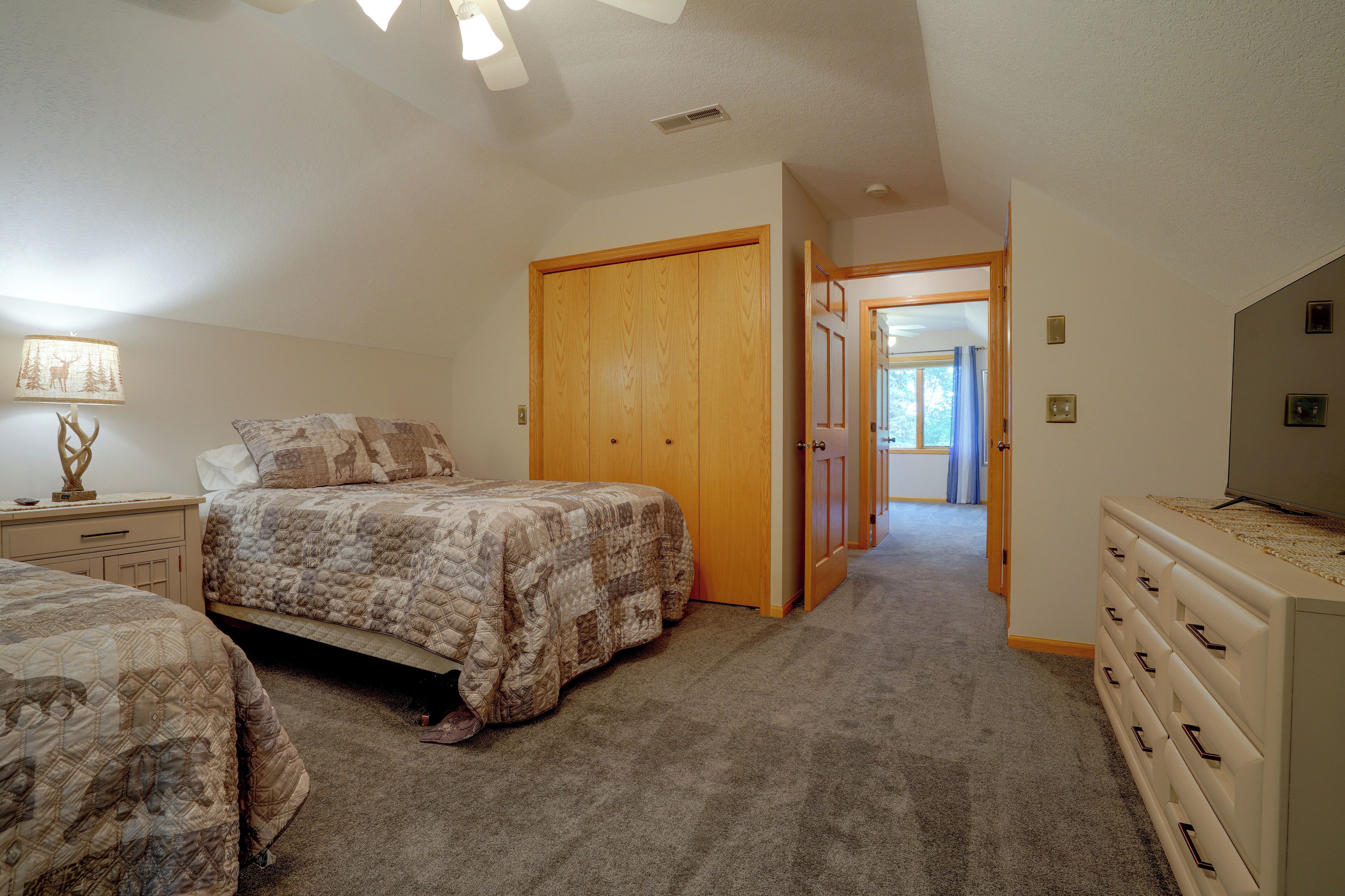 A bedroom with two beds, a dresser, and a door leading to another room.