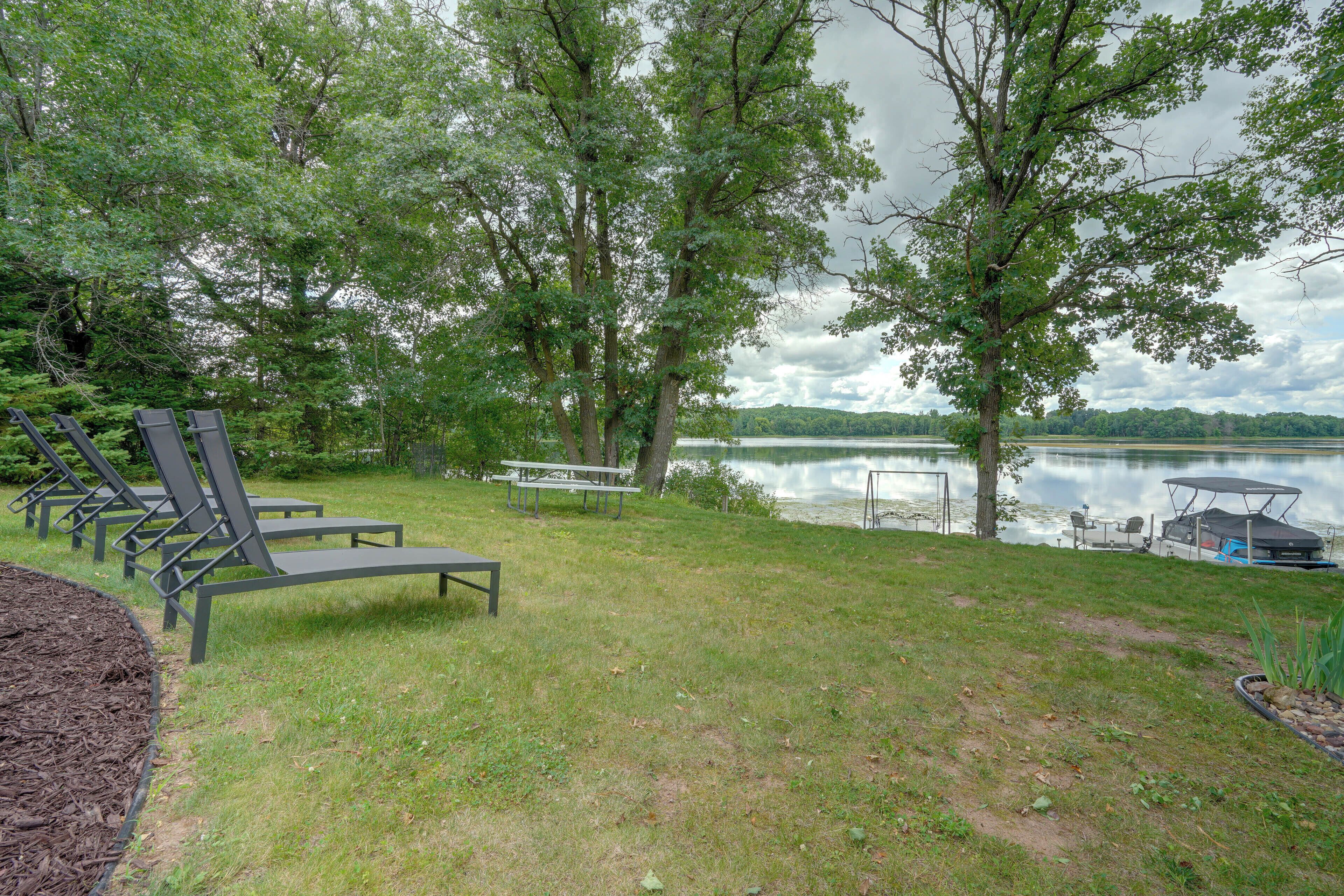 A lakeside outdoor seating area with lounge chairs and a picnic table.