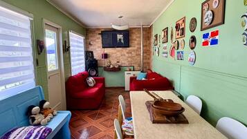 A compact living space with a dining area, a red sofa, a blue bench, and a television mounted on the wall.