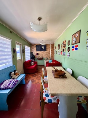 Un espacio habitable compacto con zona de comedor, un sofá rojo, un banco azul y un televisor montado en la pared.