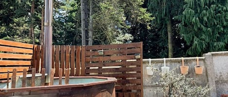 A hot tub with a wooden deck, surrounded by a wooden fence and trees.