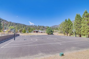 Una cancha de baloncesto al aire libre, con cielo despejado, rodeada de árboles y edificios.