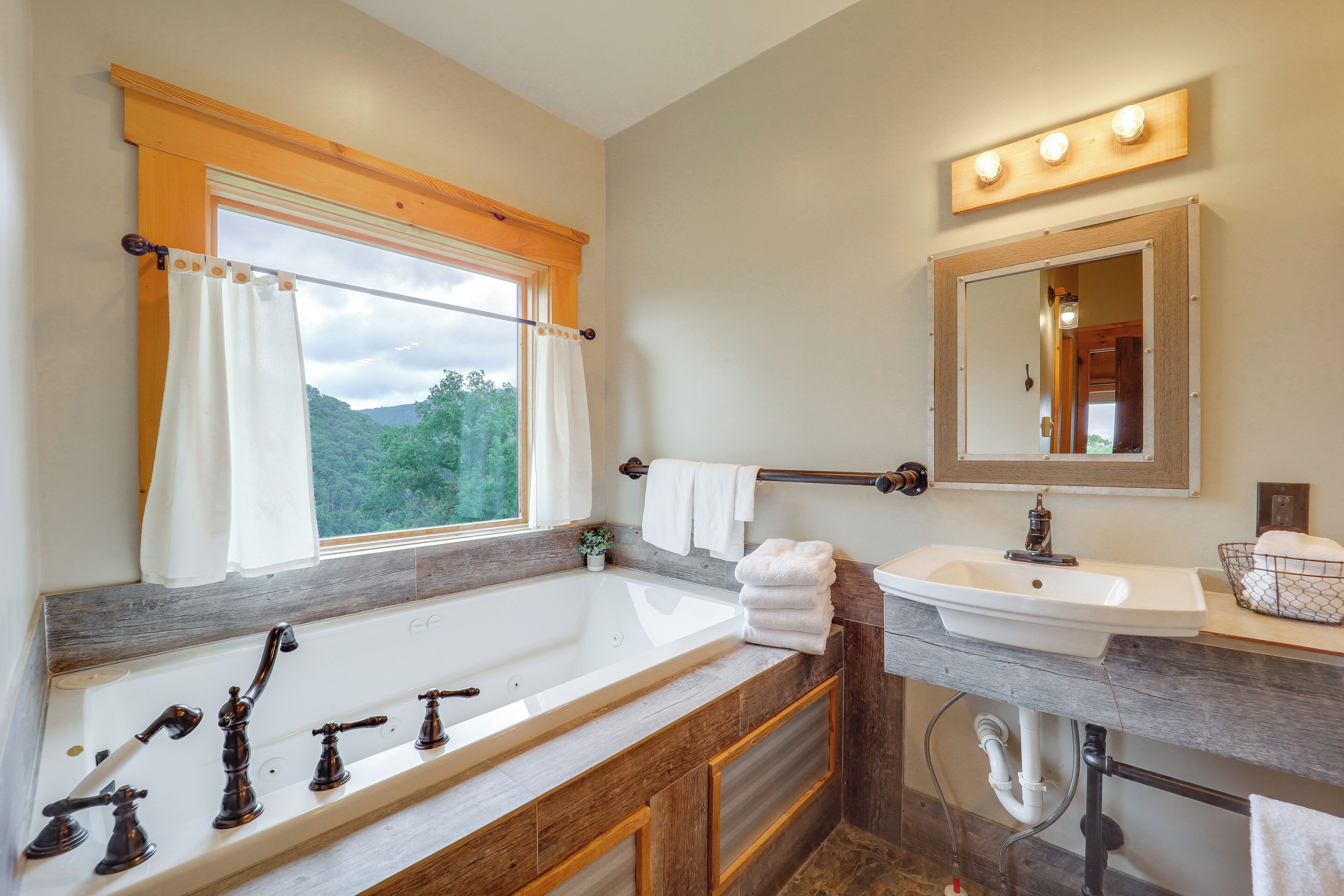 A bathroom with a bathtub, a sink, a mirror, and a window with curtains.