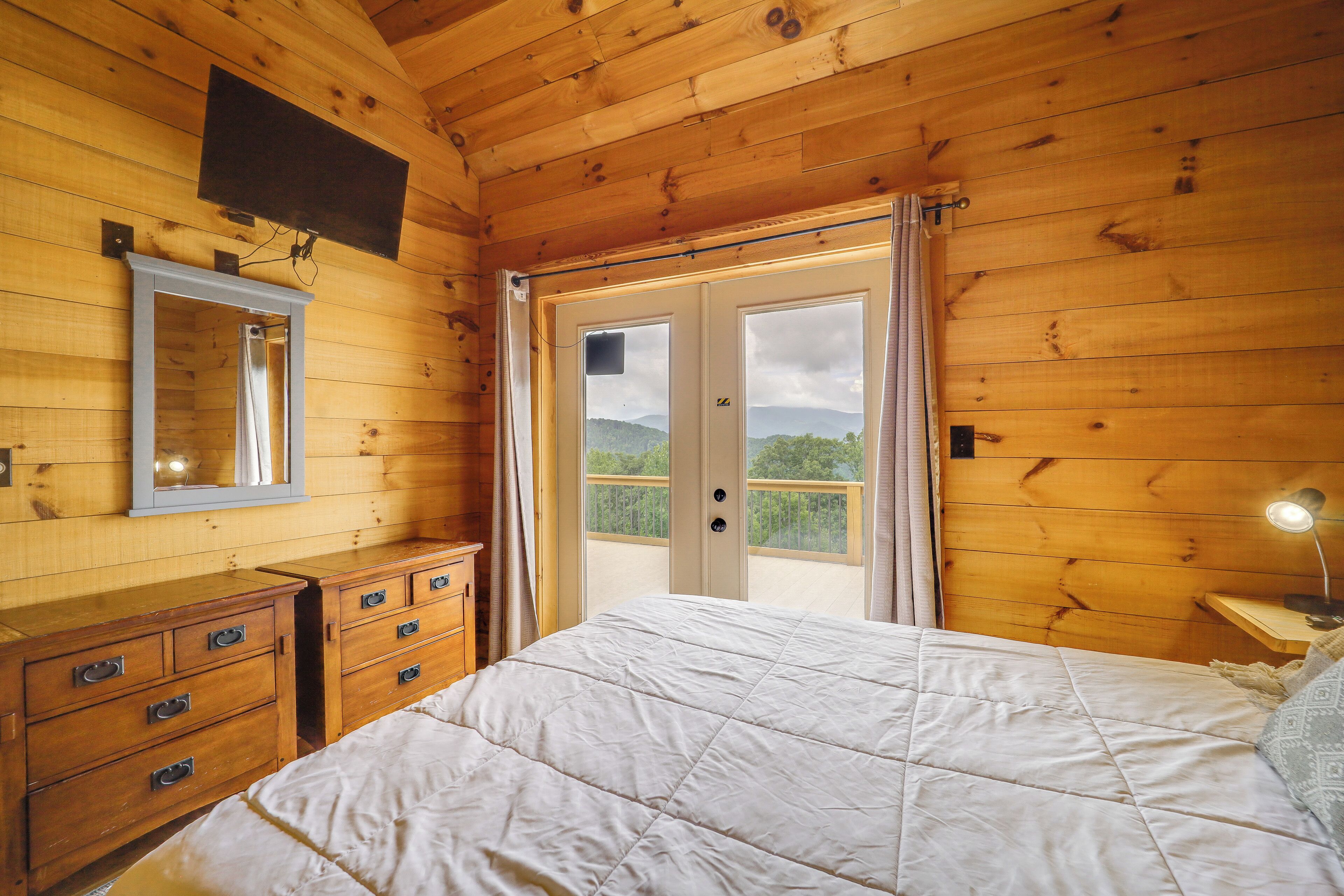 Una habitación con piso de madera, una cama, un tocador, un espejo y una puerta que da a un balcón.