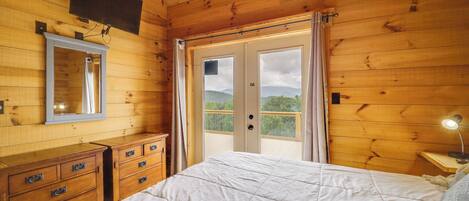 Una habitación con piso de madera, una cama, un tocador, un espejo y una puerta que da a un balcón.