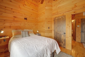 A wooden cabin bedroom with a bed, bedside lamps, and a door. - 66-acre Group Escape! Gateway to Grandfather Mtn (Elk Park)