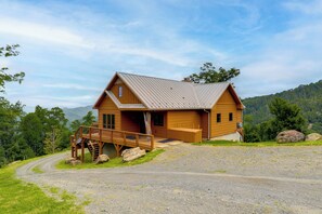 A wooden cabin with a porch and a staircase leading to a deck, surrounded by a gravel driveway and lush greenery. - 66-acre Group Escape! Gateway to Grandfather Mtn (Elk Park)