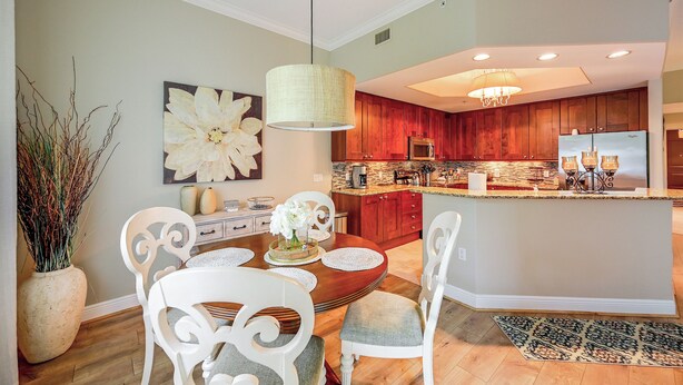 Una cocina moderna con armarios de madera, una isla central y un comedor con sillas blancas y una mesa.