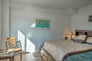 A bedroom with a bed, a chair, a table, and a wall-mounted picture.