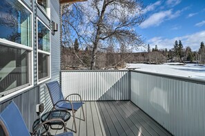 A wooden deck with metal railings, a chair, and a view of a snowy landscape and trees.