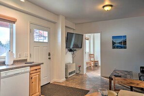 A kitchen with a dishwasher, a flat-screen TV mounted on the wall, and a dining area with a table and chairs. - Northern Lights View! 2-unit 'fitz Creek Retreat' (Homer)