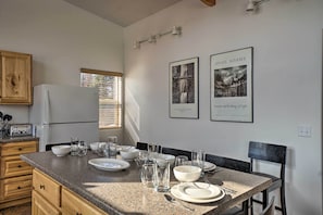 A kitchen with granite countertops, wooden cabinets, and a dining area with a table set for four. There are framed pictures on the wall and a window with blinds. - Northern Lights View! 2-unit 'fitz Creek Retreat' (Homer)
