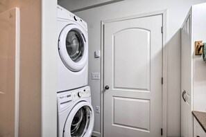 A laundry room with stacked washers and dryers, a white door, and a small electrical outlet. - Northern Lights View! 2-unit 'fitz Creek Retreat' (Homer)