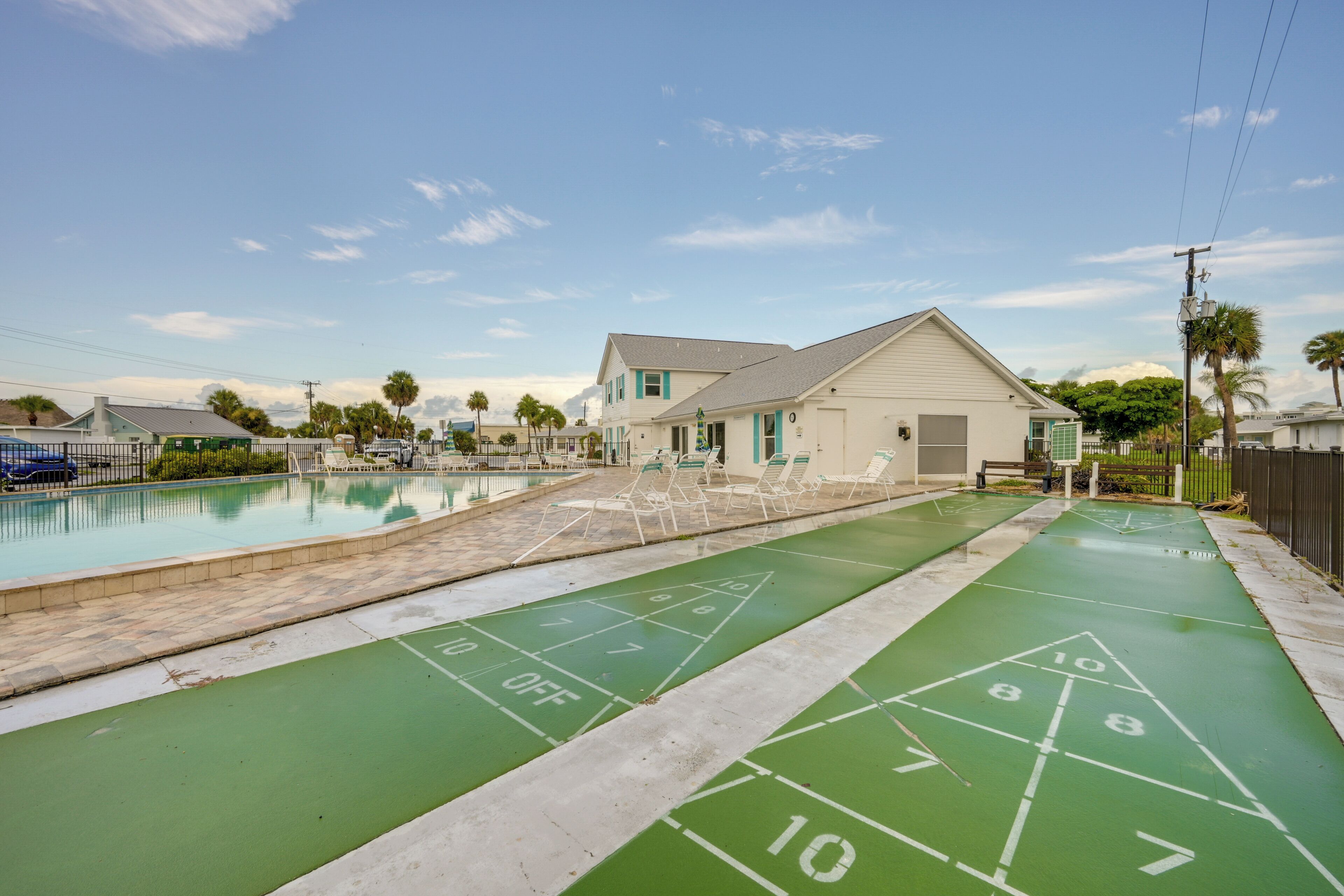 A pool area with a shuffleboard court and a building with a white exterior.