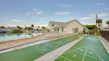 A pool area with a shuffleboard court and a building with a white exterior.