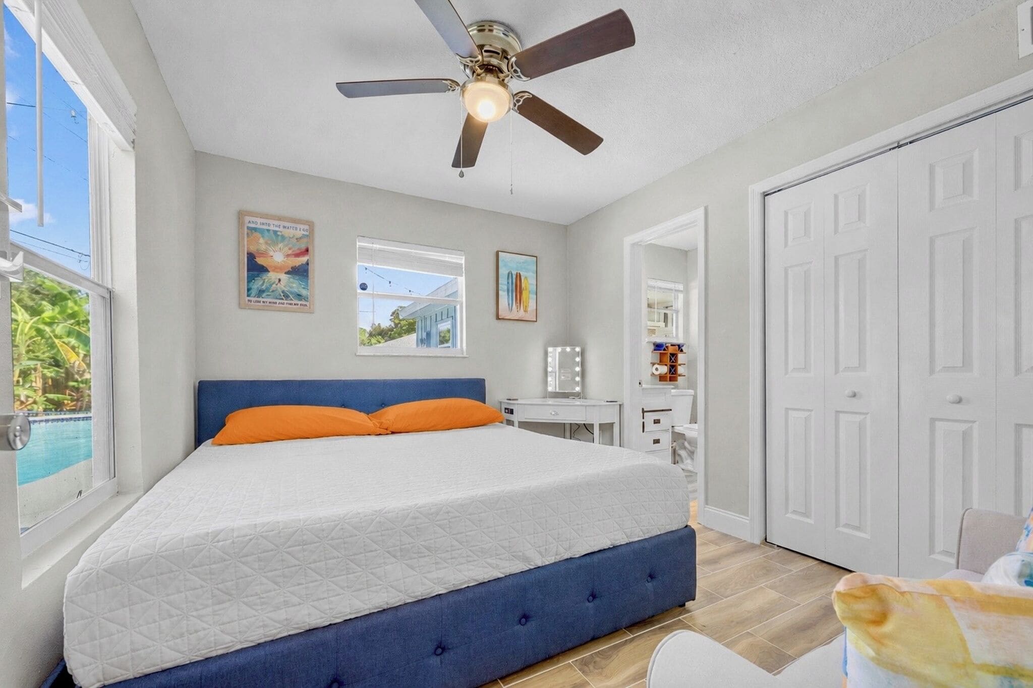 Un dormitorio con cama, ventilador de techo, ventana con vistas y una puerta.