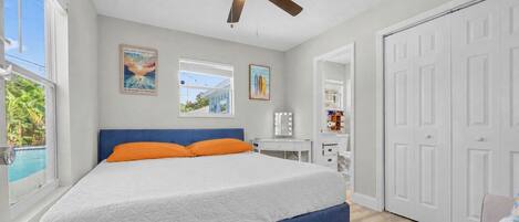 Un dormitorio con cama, ventilador de techo, ventana con vistas y una puerta.