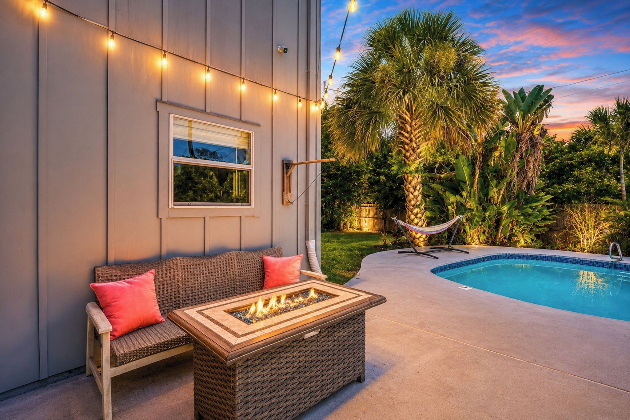 An outdoor patio with a wicker sofa, a fire pit, a hammock, and a swimming pool.