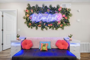 A bedroom with a neon sign, a bed with two pillows, a wall-mounted plant, and a white door. - 13 Mi to Beach! Family-friendly Palm Bay Retreat (Palm Bay)