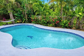 A swimming pool with a tiled edge, surrounded by lush greenery and a wooden fence. - 13 Mi to Beach! Family-friendly Palm Bay Retreat (Palm Bay)