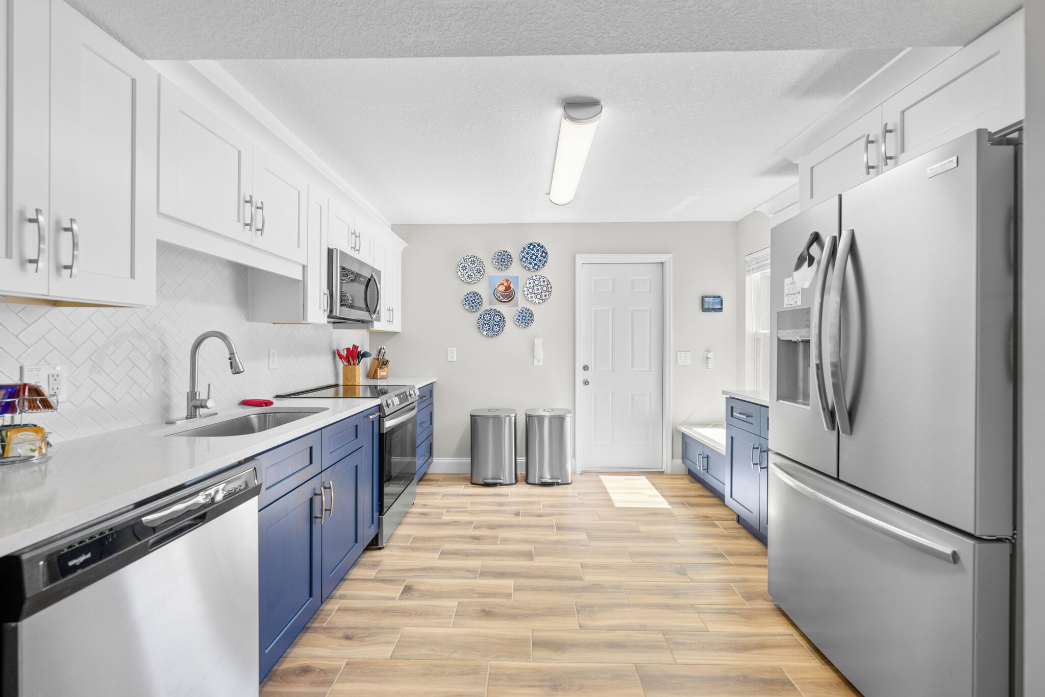 A modern kitchen with white cabinets, stainless steel appliances, and a herringbone wood floor.