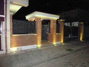 Edificio residencial con fachada de ladrillo, entrada protegida por una reja y un porche bien iluminado.