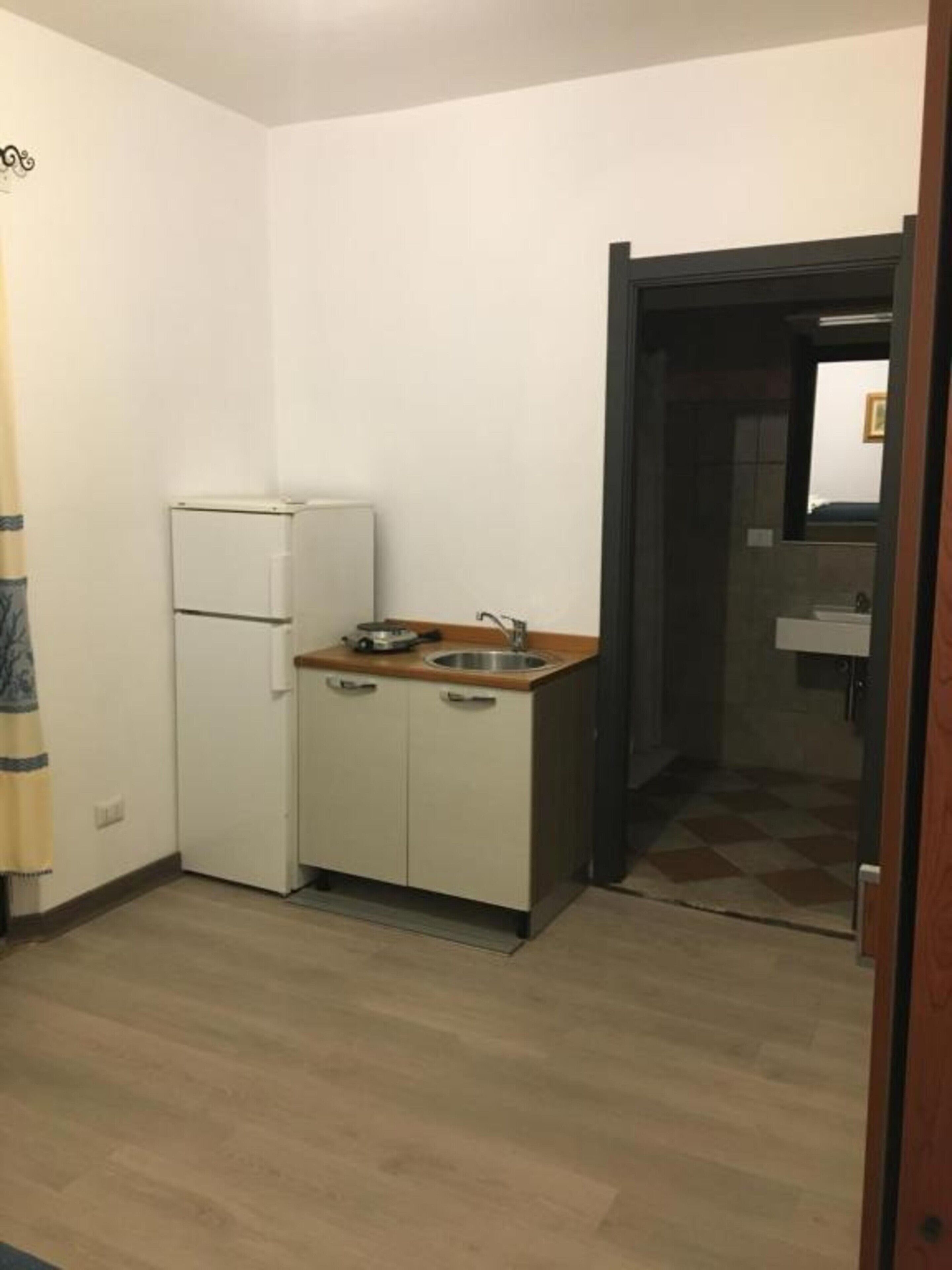 Een kleine keuken met een koelkast, een wastafel en kastjes.
