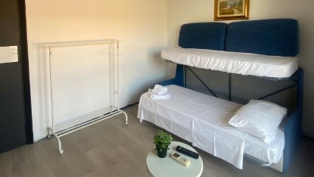 Quarto com uma cama beliche, uma pequena mesa redonda com uma planta, um quadro na parede e um ar condicionado.
