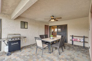 Eine Terrasse im Freien mit Grill, Esstisch, Stühlen und Deckenventilator.