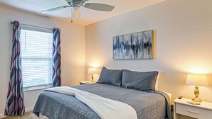 A bedroom with a bed, two bedside tables, a ceiling fan, a window with curtains, and a wall-mounted abstract painting. - Community Pools, Golf & More! Home in The Villages (Wildwood)