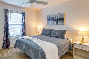 A bedroom with a bed, two bedside tables, a ceiling fan, a window with curtains, and a wall-mounted abstract painting. - Community Pools, Golf & More! Home in The Villages (Wildwood)
