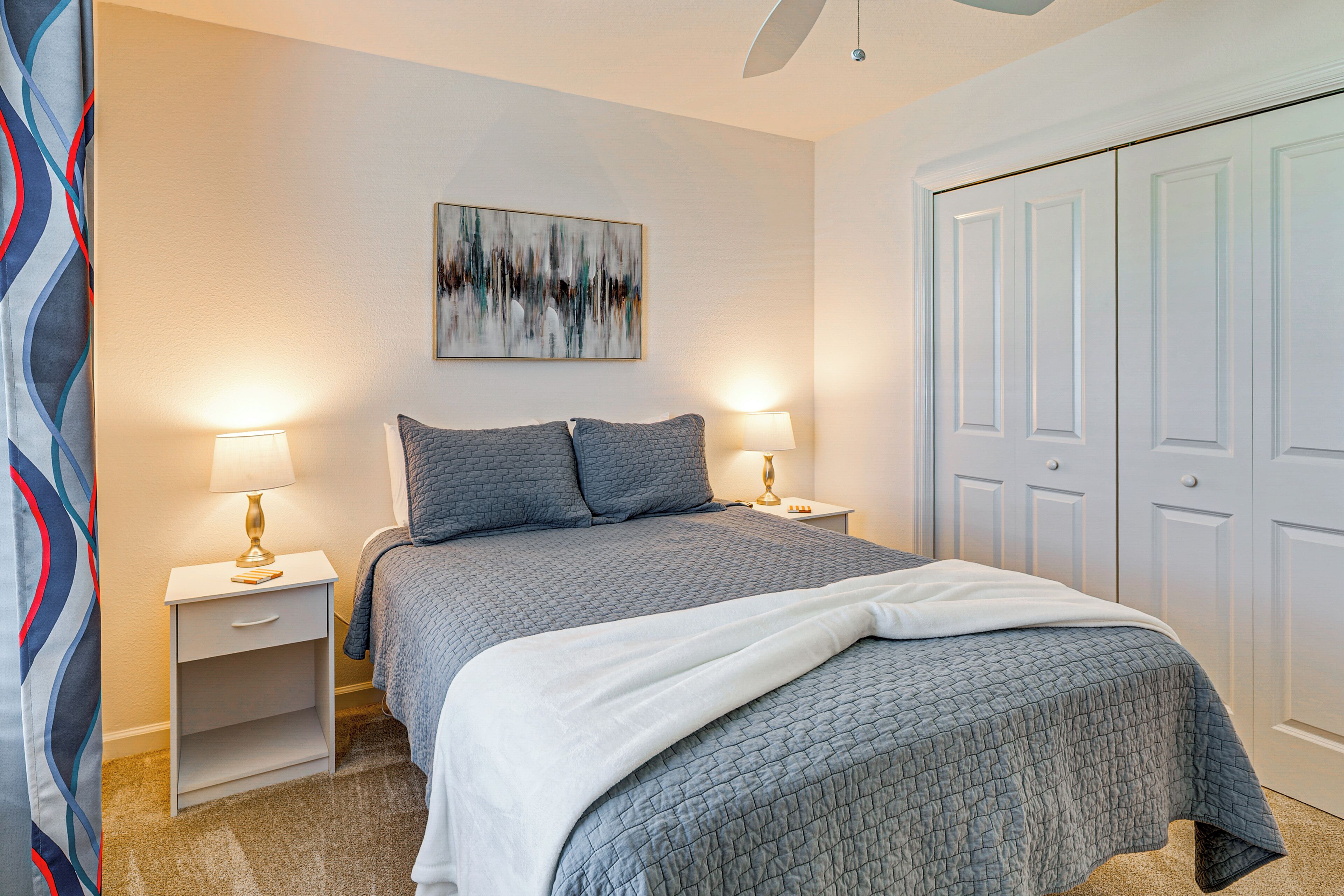 Une chambre à coucher avec un lit, deux tables de chevet avec des lampes, un tableau au mur et une armoire.