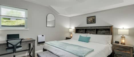 A bedroom with a bed, bedside lamps, a desk with a chair, a window, and a mirror.