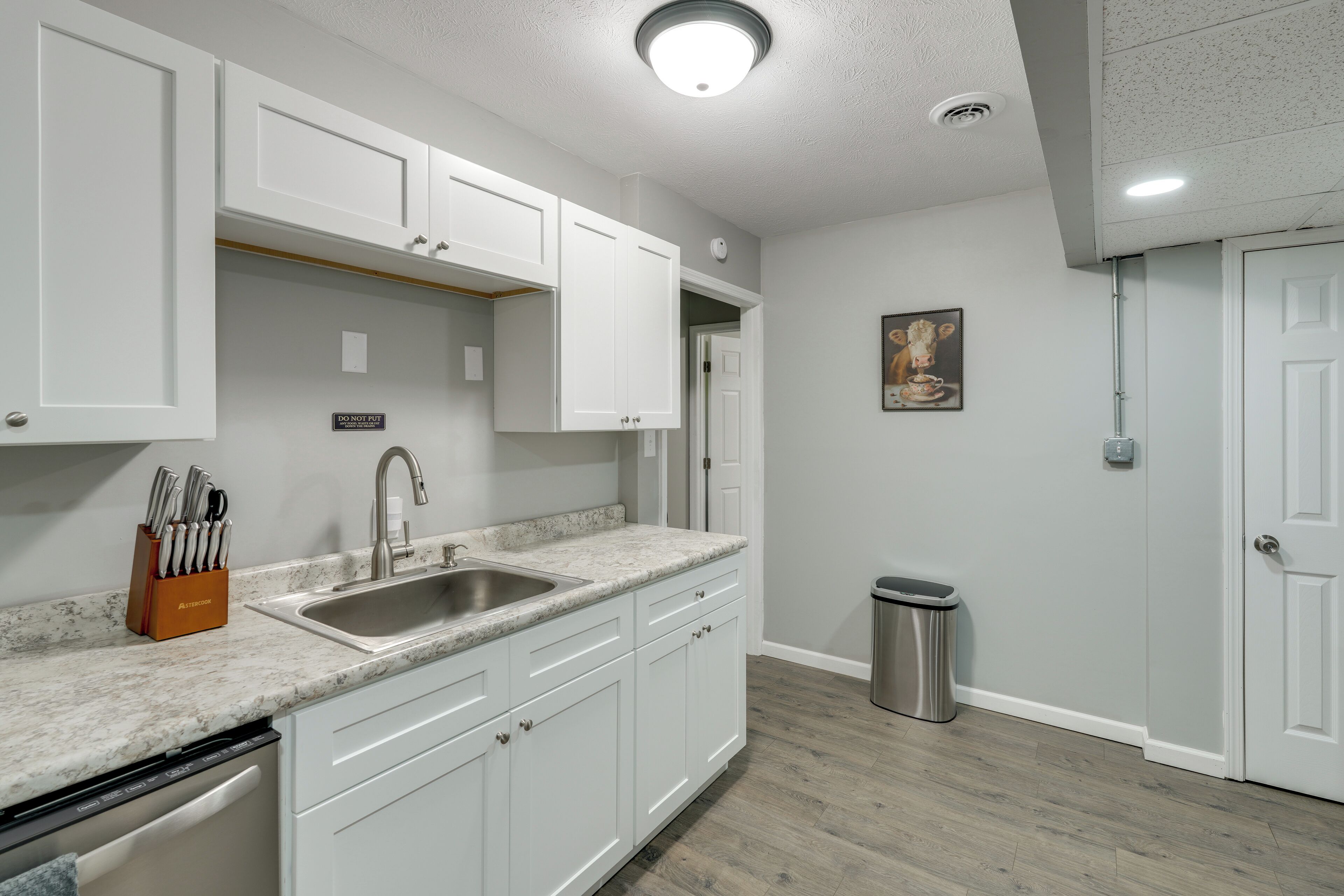 A modern kitchen with white cabinets, a stainless steel sink, and a marble countertop.
